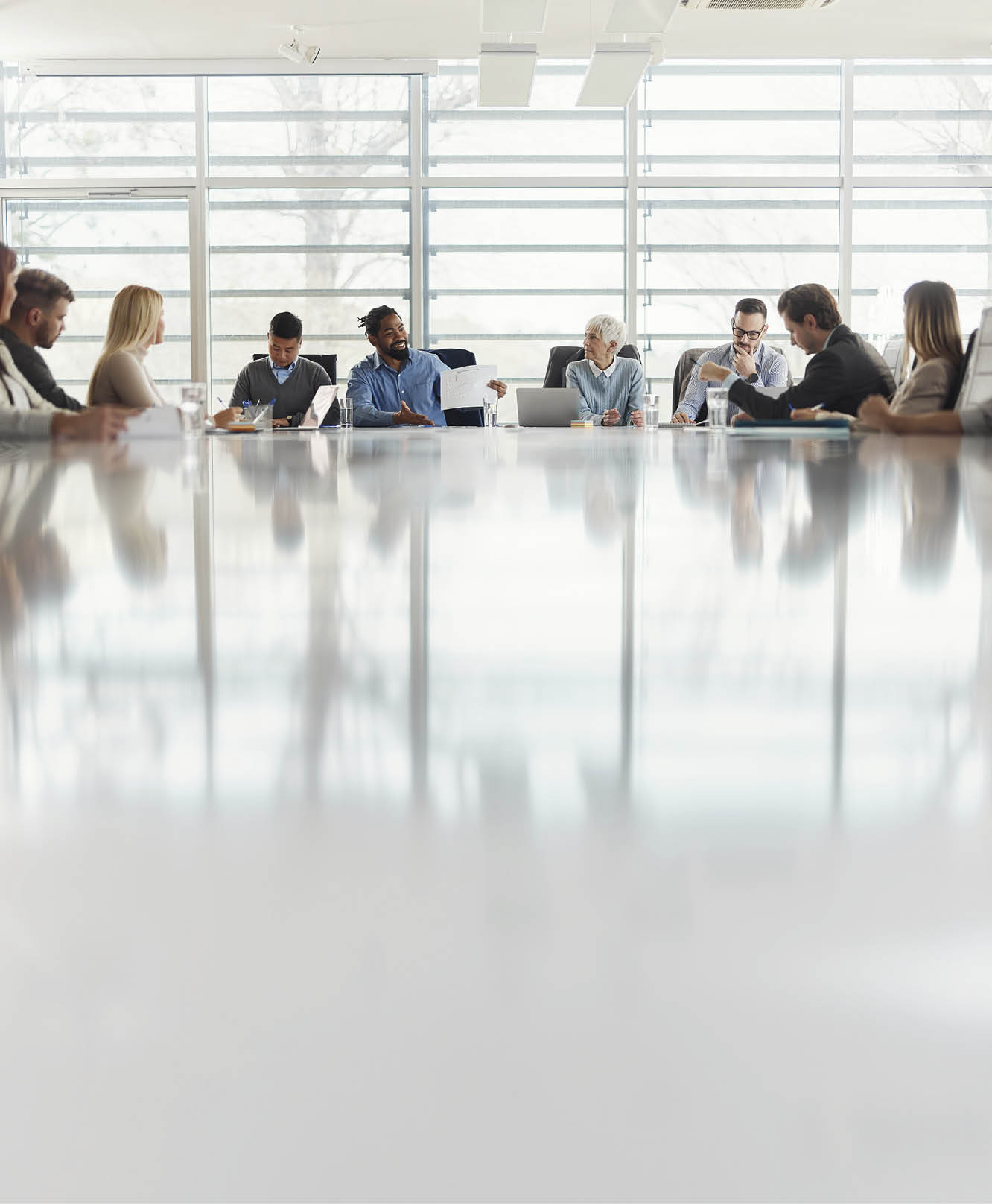 Happy African American entrepreneur talking about business charts to a large group of his colleagues on a meeting at conference table. Copy space.