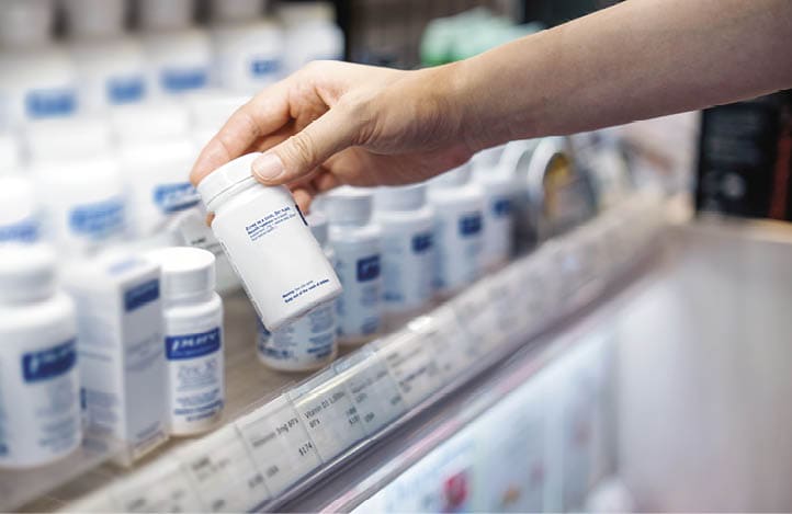 Cropped shot of young Asian woman's hand taking a bottle of medicine from the shelf at the pharmacy, reading the product information. Healthcare, medication and people concept