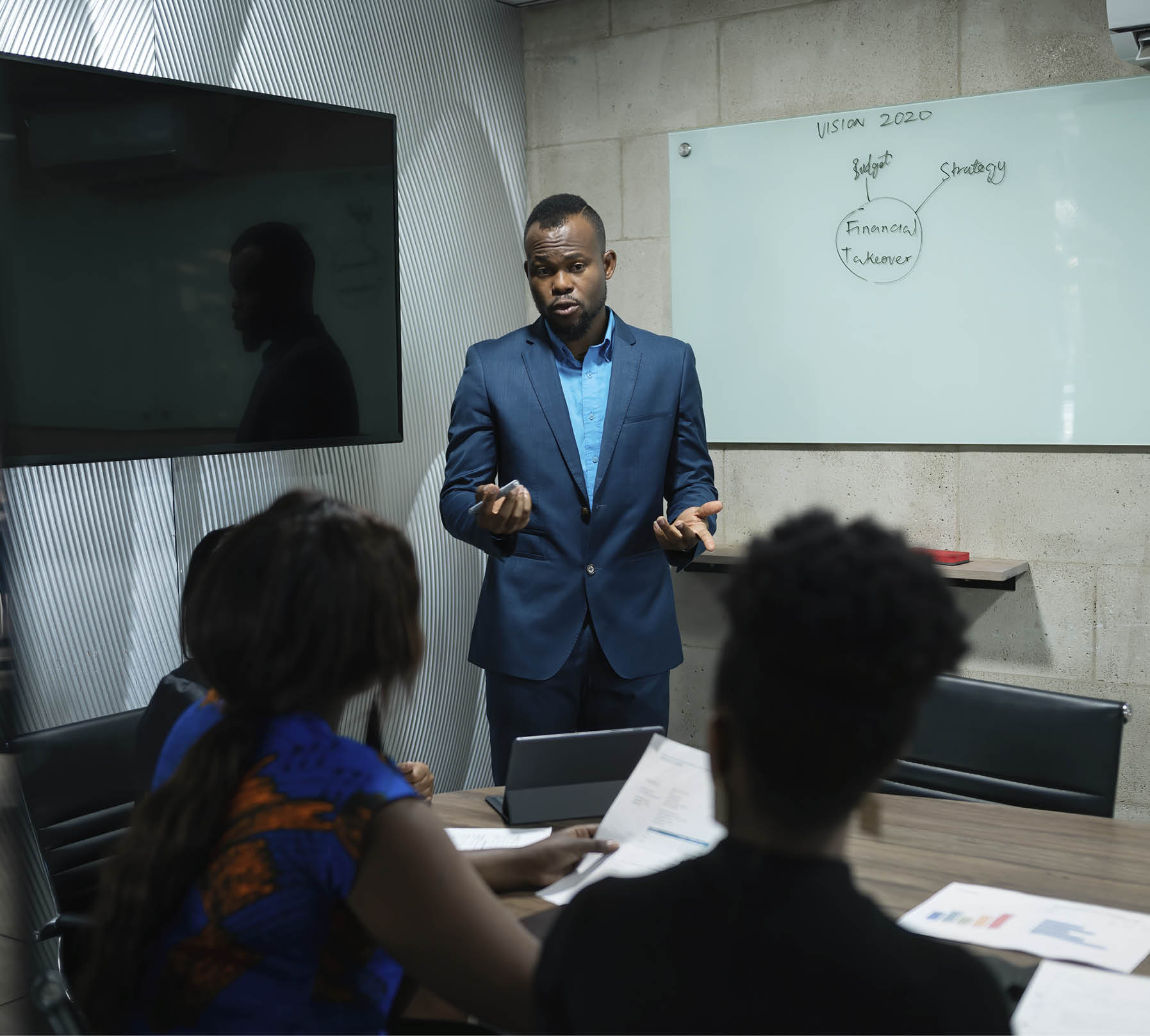 Young African businessman giving a whiteboard presentation to a group of colleagues in the boardroom of a modern office