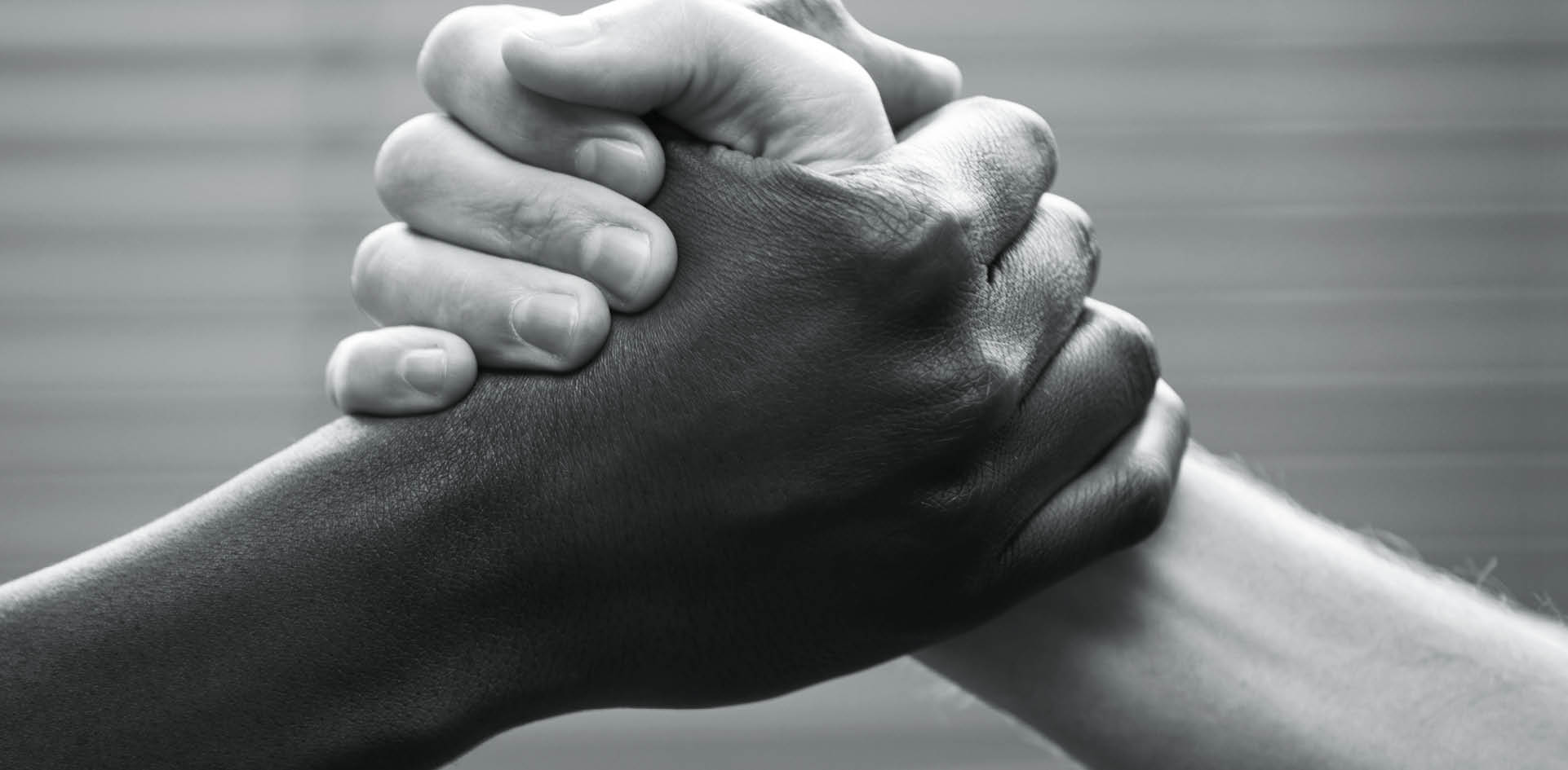 Black and white hands clasped, with blurred office blinds as backdrop.This is an African gesture of greeting and friendship but it will double for arm-wrestling, symbolizing competition or rivalry. Camera: Canon 5D.More in this series: