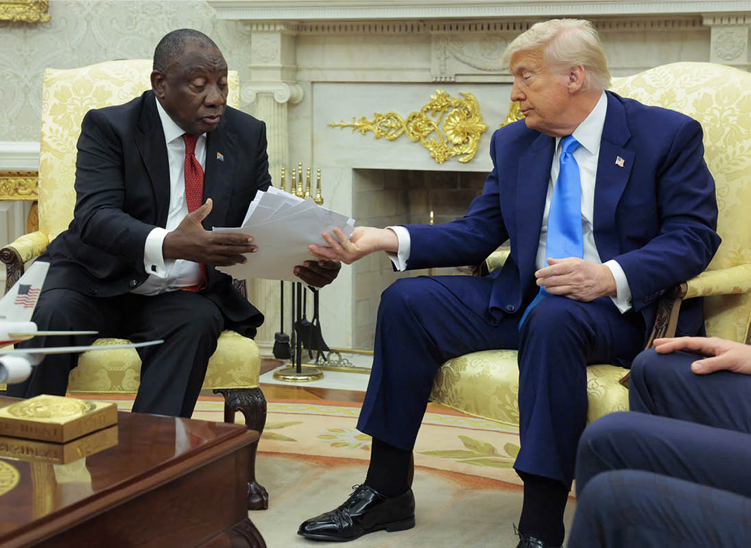 WASHINGTON, DC - MAY 21: lU.S. President Donald Trump hands President of South Africa Cyril Ramaphosa (L) articles he says report violence against white South Africans during a meeting in the Oval Office of the White House on May 21, 2025 in Washington, DC. Relations between the two countries have been strained since Trump signed an executive order in February that claimed white South Africans are the victims of government land confiscation and race-based “genocide” while admitting some of those Afrikaners as refugees to the United States. Trump also halted all foreign aid to South Africa and expelled the country’s Ambassador to the U.S. Ebrahim Rasool. (Photo by Chip Somodevilla/Getty Images)