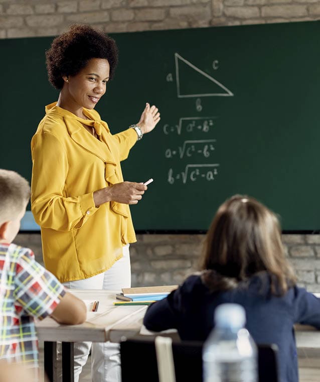 Happy African American teacher talking to school children while explaining them mathematic on a class in the classroom.