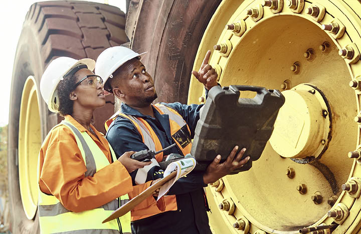 Two African Mine workers are discussing maintenance on a large haul dump truck