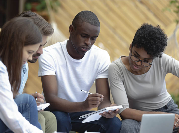 Beautiful smart girls handsome clever guys sitting in cozy place studying writing notes thoughts in notepad. Skilled man helps to teammates understand lecture learn preparing for examination together