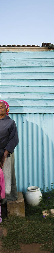 A rural African woman and her child standing in front of their house 