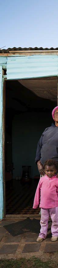 A rural African woman and her child standing in front of their house 