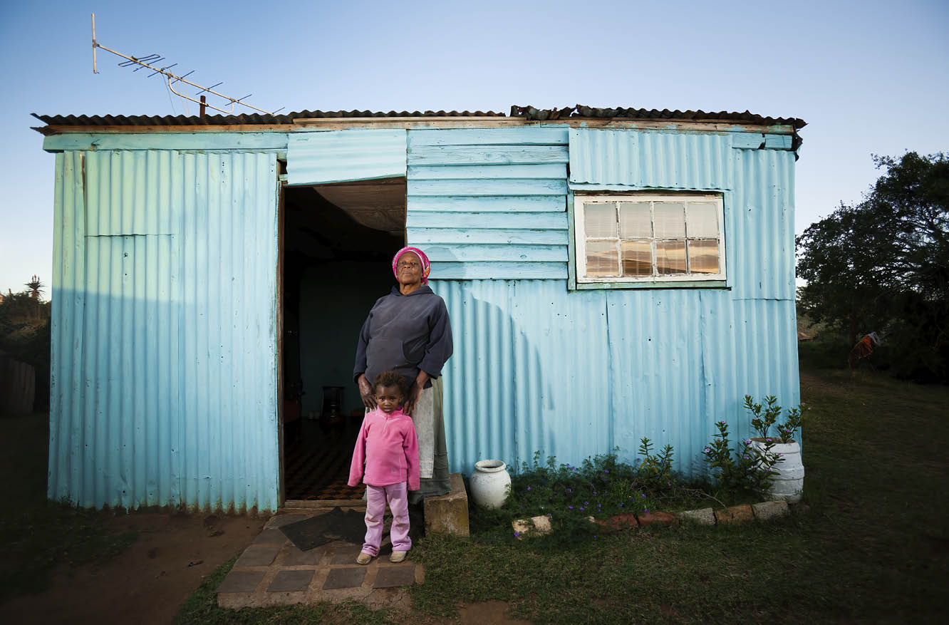 A rural African woman and her child standing in front of their house 