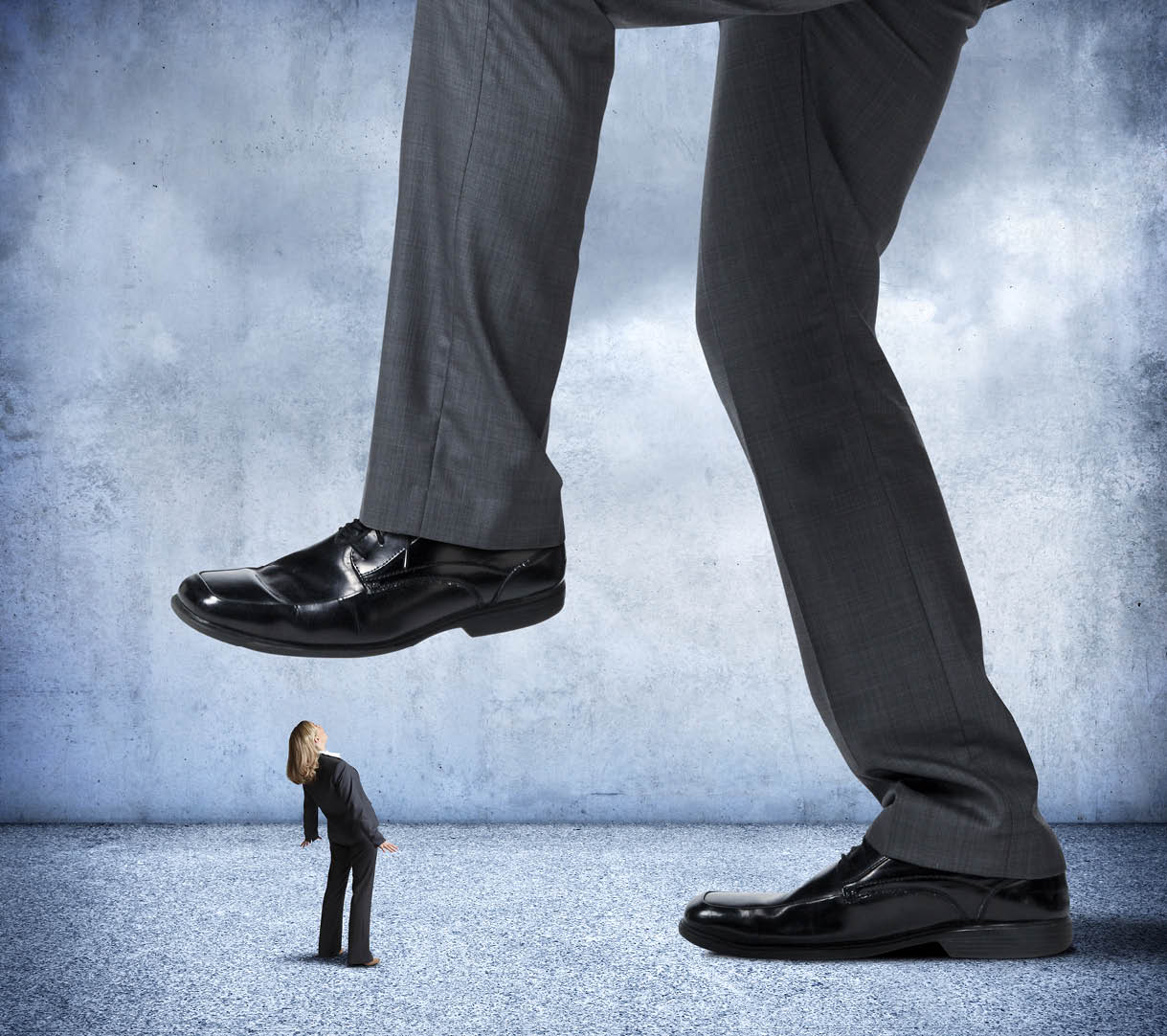 A small businesswoman looks up as she is about to get stepped on by a very large businessman.
