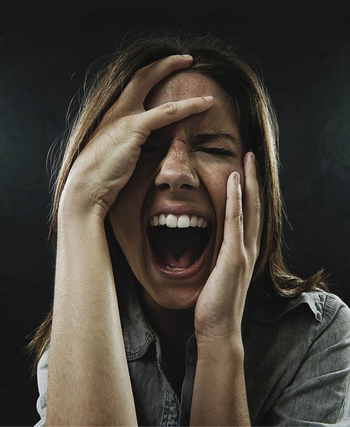A young woman screaming uncontrollably while isolated on a black background