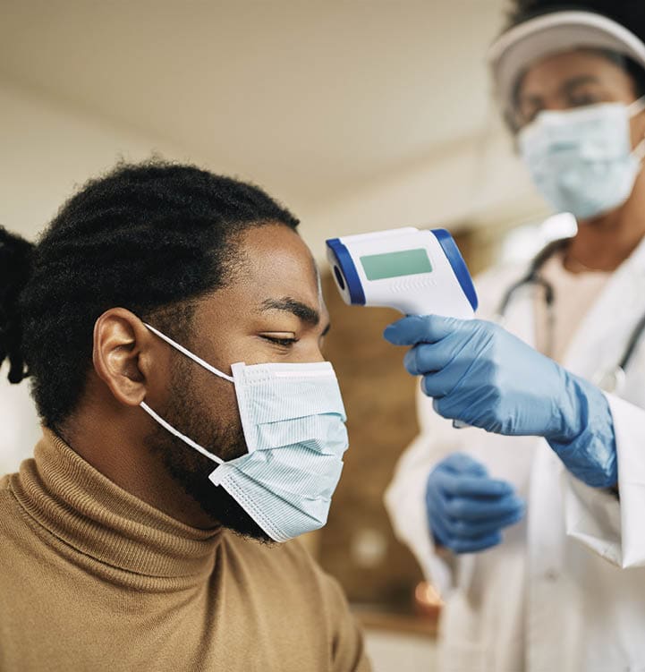 Female doctor measuring temperature of African American man with infrared thermometer while visiting him at home during coronavirus pandemic. Focus is on man.