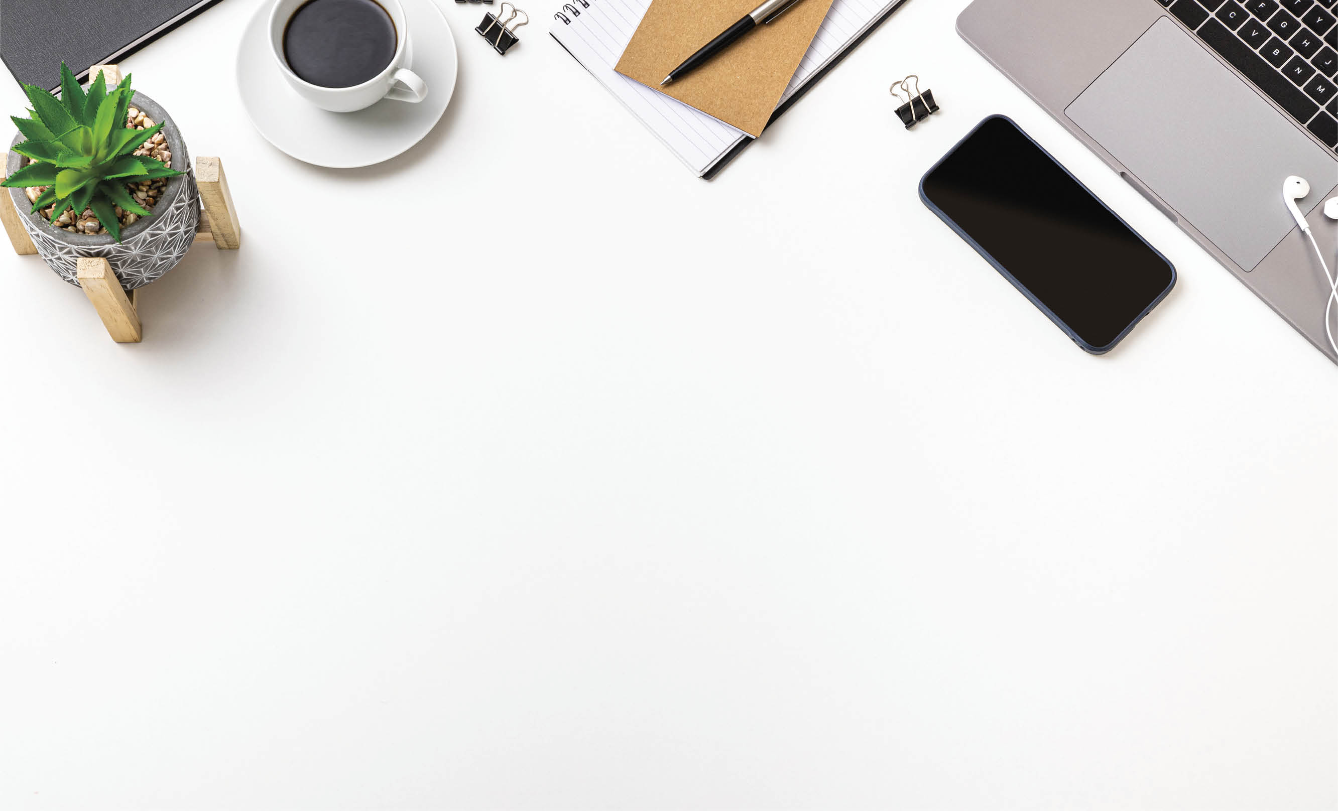 Office desk: Top view of various office supplies such as a laptop, a note pad, a coffee cup, a smartphone and a plant. All the objects are at the top of the image leaving a useful copy space at the bottom on white background.